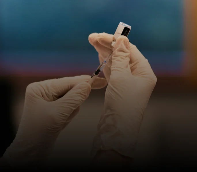 Gloved hands preparing a vaccine with syringe and vial